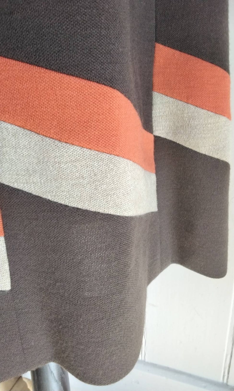 May include: Close-up of a brown, orange and beige striped fabric. The fabric has a woven texture.