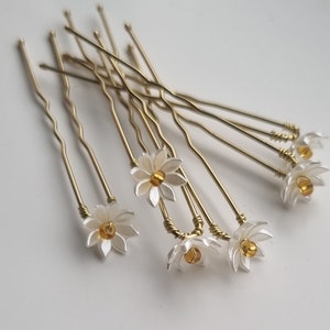 May include: A set of ten gold hair pins with white flower accents and amber colored beads in the center of each flower.