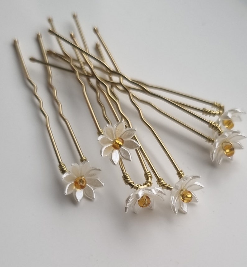 May include: A set of ten gold hair pins with white flower accents and amber colored beads in the center of each flower.