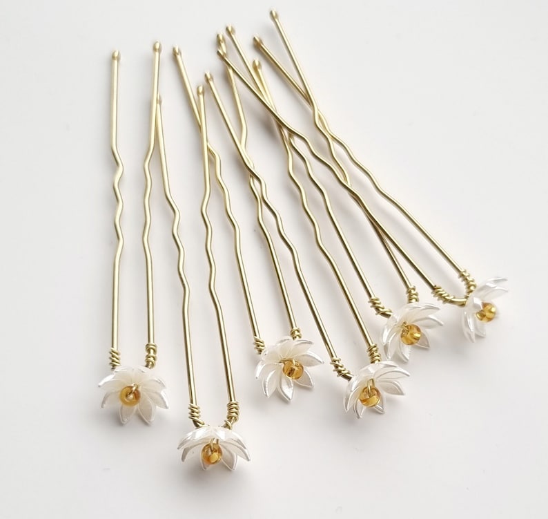 May include: Set of eight gold hair pins with white flower accents. Each pin has a delicate flower design with a gold center.