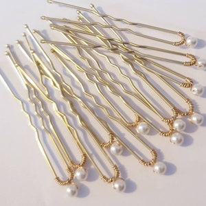 May include: A set of gold hair pins with white pearl accents. The pins are wavy and have a loop at the end with a pearl attached.