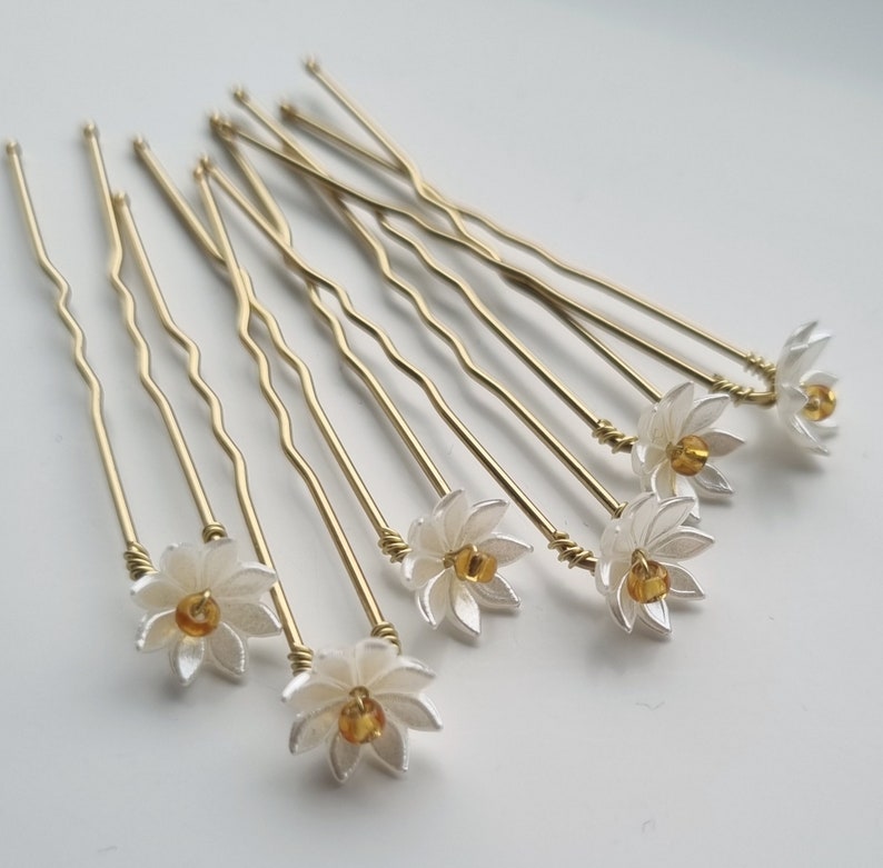 May include: Set of ten gold hair pins with white flower accents and a small amber bead in the center of each flower.