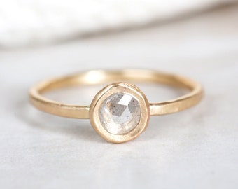 May include: A gold ring with a round, clear, faceted gemstone set in a bezel setting.
