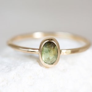 May include: A delicate gold ring with a green oval gemstone set in a bezel setting.