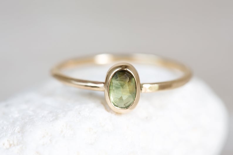May include: A delicate gold ring with a green oval gemstone set in a bezel setting.