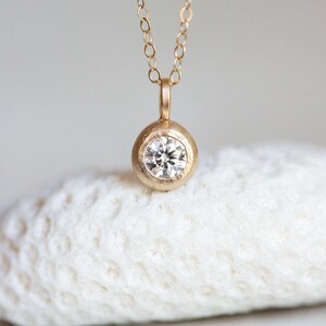 May include: A delicate gold necklace with a round pendant featuring a small, clear diamond.