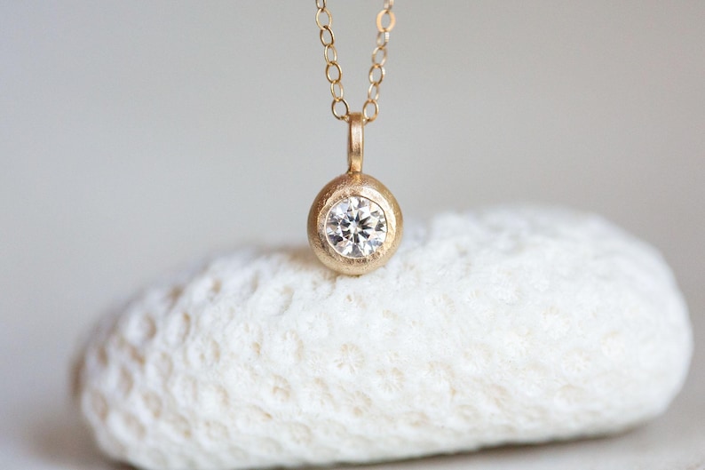 May include: A delicate gold necklace with a round pendant featuring a small, clear diamond.