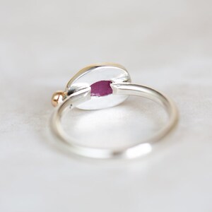 May include: A silver ring with a gold accent and a pink oval stone. The ring is set on a white background.