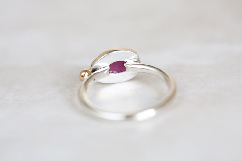 May include: A silver ring with a gold accent and a pink oval stone. The ring is set on a white background.