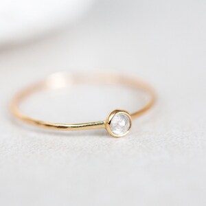 Pode incluir: Um delicado anel de ouro com um &uacute;nico diamante pequeno, redondo e transparente.