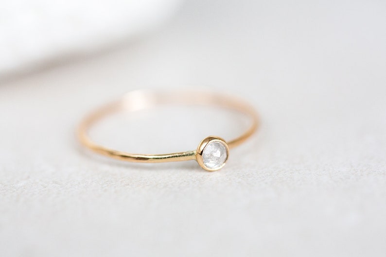 Pode incluir: Um delicado anel de ouro com um &uacute;nico diamante pequeno, redondo e transparente.