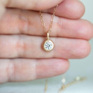May include: A delicate gold chain necklace with a small, round, bezel-set diamond pendant.