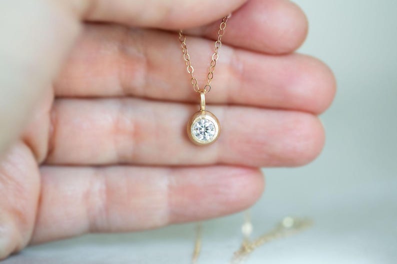 May include: A delicate gold chain necklace with a small, round, bezel-set diamond pendant.