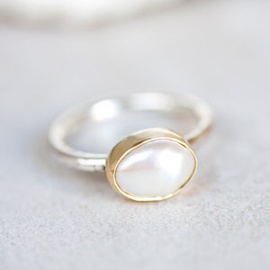 May include: A silver ring with a gold setting and a white pearl.