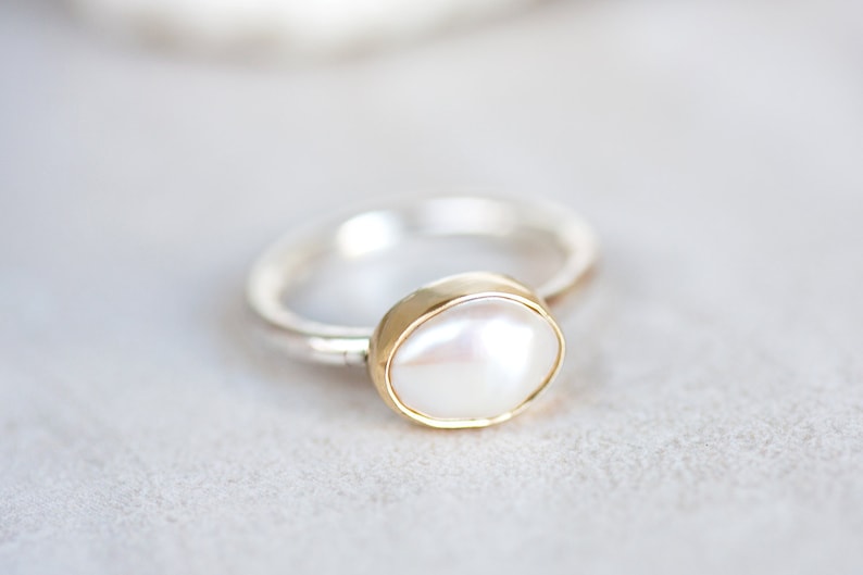 May include: A silver ring with a gold setting and a white pearl.