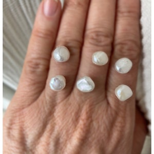 May include: Six white, irregular shaped pearls on a hand.