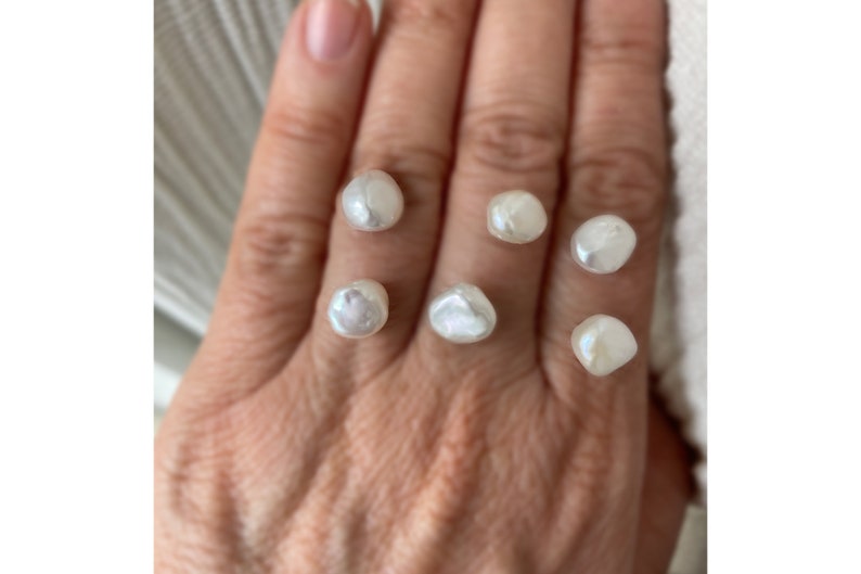 May include: Six white, irregular shaped pearls on a hand.