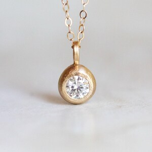May include: A gold pendant necklace with a round, textured setting that holds a clear, round diamond.