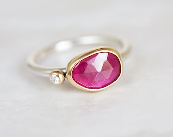May include: A ring with a large, faceted, pink gemstone set in a gold bezel. A smaller, round, clear gemstone is set in a gold bezel on the band.
