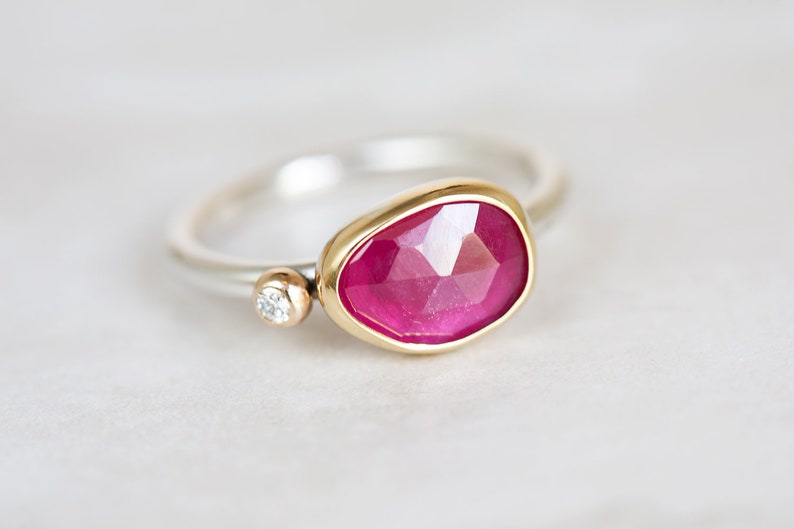 May include: A ring with a large, faceted, pink gemstone set in a gold bezel. A smaller, round, clear gemstone is set in a gold bezel on the band.