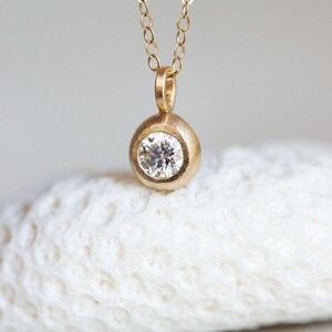 May include: A gold necklace with a round pendant featuring a single, clear diamond.