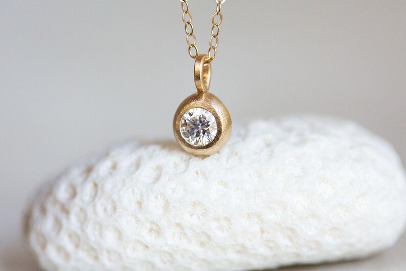 May include: A gold necklace with a round pendant featuring a single, clear diamond.