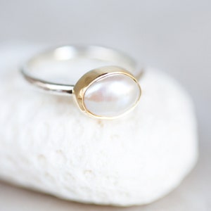 May include: A silver ring with a gold setting and a white pearl.