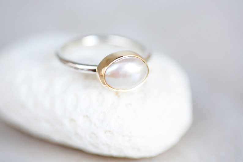 May include: A silver ring with a gold setting and a white pearl.