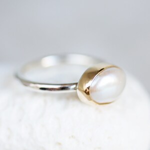 May include: A silver ring with a gold setting and a white pearl.