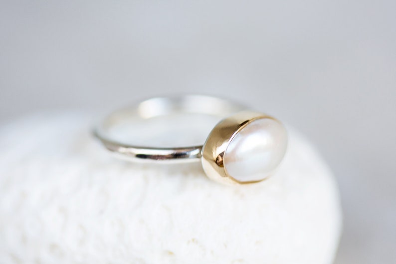 May include: A silver ring with a gold setting and a white pearl.