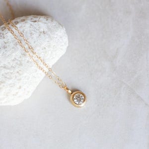 May include: A delicate gold chain necklace with a small, round, clear gemstone pendant.