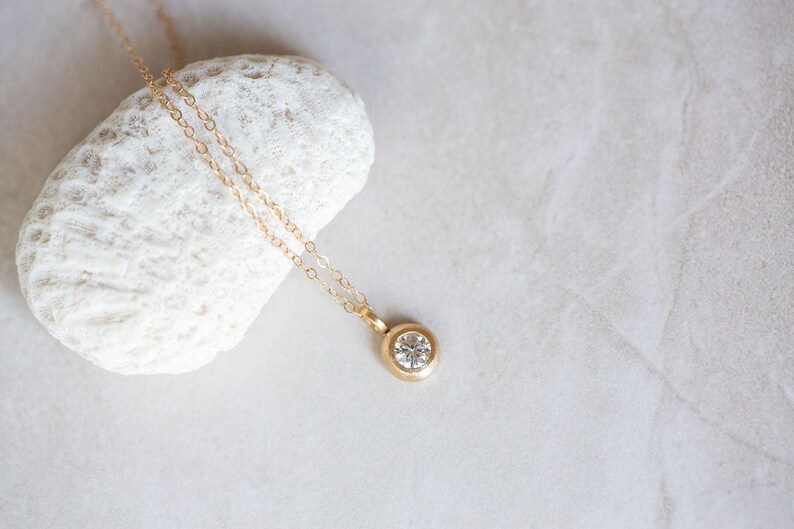 May include: A delicate gold chain necklace with a small, round, clear gemstone pendant.