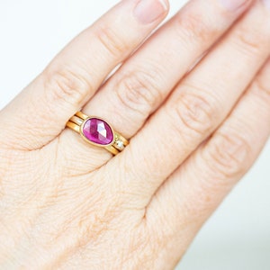 May include: A gold ring with a pink gemstone set in a bezel setting. The ring is worn on a finger.