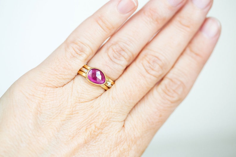 May include: A gold ring with a pink gemstone set in a bezel setting. The ring is worn on a finger.