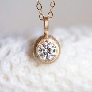 May include: A delicate gold necklace with a round pendant featuring a small, clear diamond.