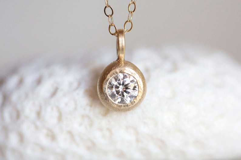 May include: A delicate gold necklace with a round pendant featuring a small, clear diamond.