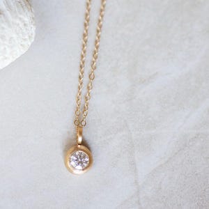 May include: A delicate gold chain necklace with a small round pendant featuring a clear gemstone.