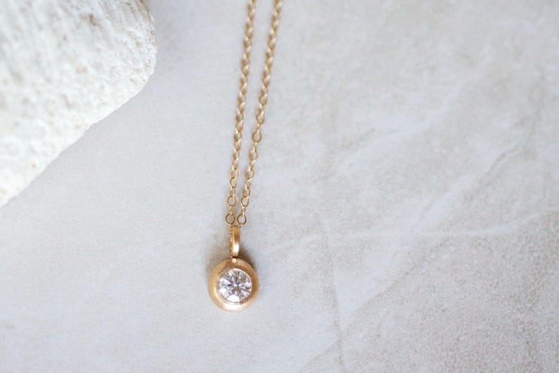 May include: A delicate gold chain necklace with a small round pendant featuring a clear gemstone.
