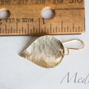May include: A gold leaf-shaped earring with a hammered texture and a wire hook closure. The earring is labeled "Medium".