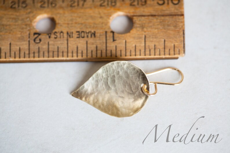 May include: A gold leaf-shaped earring with a hammered texture and a wire hook closure. The earring is labeled "Medium".