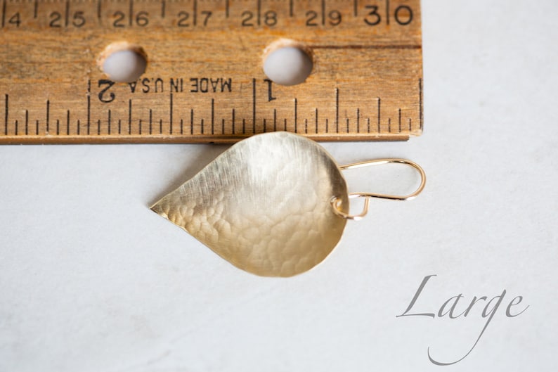 May include: A gold teardrop-shaped earring with a hammered texture. The earring is approximately 1 inch long and is shown next to a ruler. The word "Large" is written below the earring.
