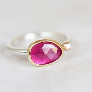 May include: A silver ring with a pink gemstone set in a gold bezel. A small diamond is set in the band.