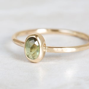 May include: A gold ring with a green gemstone set in a bezel setting. The ring band is hammered and has a textured finish.
