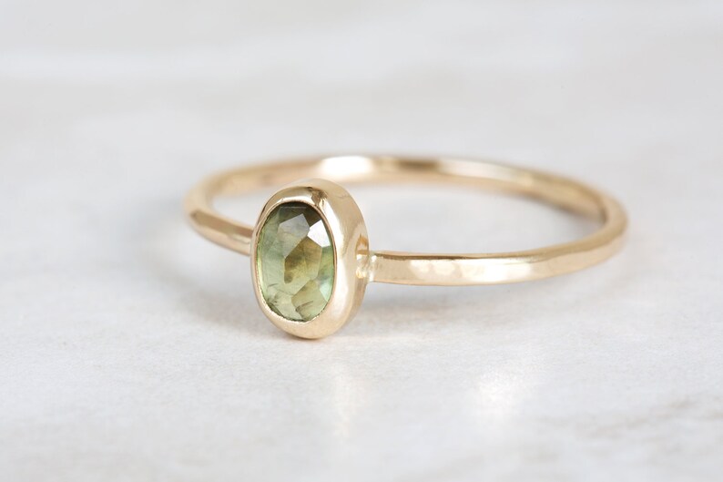 May include: A gold ring with a green gemstone set in a bezel setting. The ring band is hammered and has a textured finish.