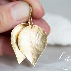May include: Gold leaf earrings with a hammered texture. The earrings are large and have a teardrop shape. The word "Large" is written in cursive below the earrings.