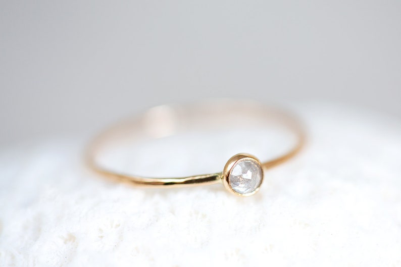 Pode incluir: Um delicado anel de ouro com um &uacute;nico diamante redondo e transparente.