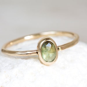 May include: A gold ring with a green oval gemstone set in a bezel setting. The ring has a hammered texture.