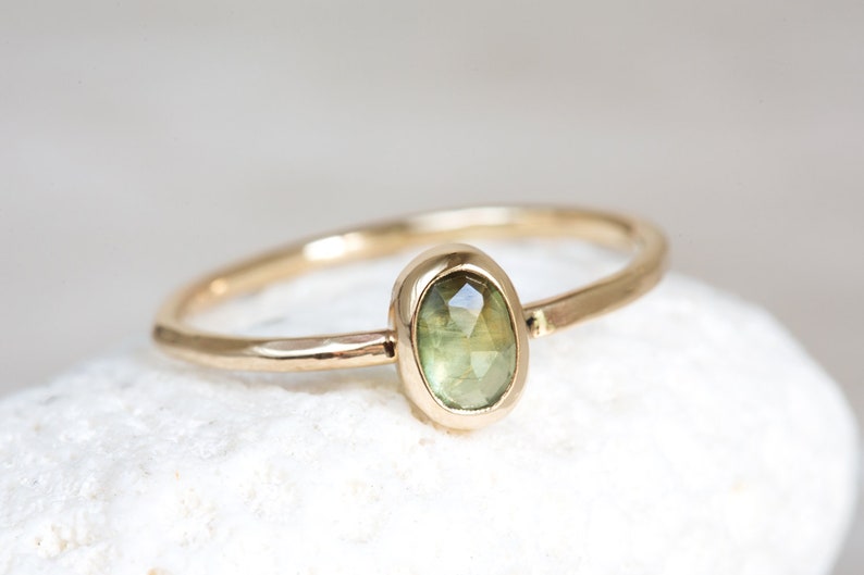 May include: A gold ring with a green oval gemstone set in a bezel setting. The ring has a hammered texture.