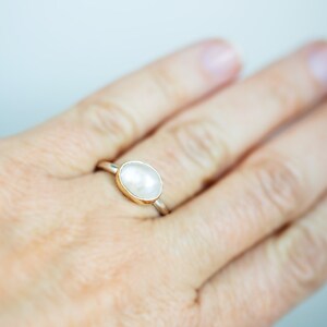 May include: A silver ring with a white oval gemstone set in a gold band.