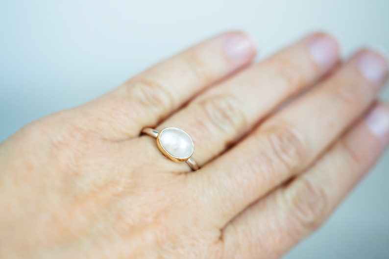 May include: A silver ring with a white oval gemstone set in a gold band.